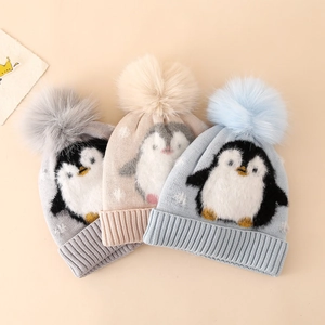 Detail of winter knit hats for boys featuring jacquard penguin patterns and fluffy pom-poms
