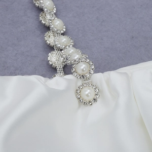 Detail of white satin dress featuring elegant pearl and rhinestone embellished straps