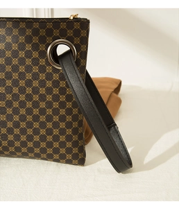 Detail of crocodile embossed dark brown clutch with golden clover pattern and leather handle