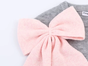 Close-up of a grey knit sweater featuring a large pink bow with soft textured wool details