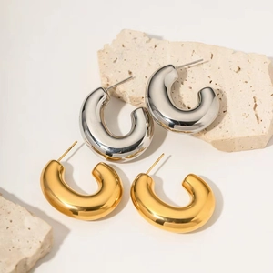 Detail of high-polish 18K gold and silver chunky C-shaped hoop earrings on stone