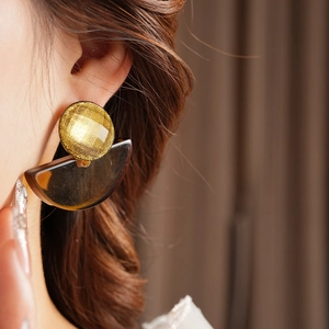 Detail of bohemian geometric resin earring with gold disc and amber fan on model