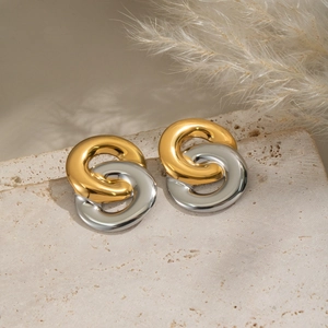 Close-up of interlocking gold and silver circle earrings on a textured stone surface