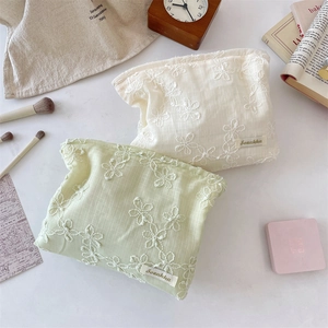 Detailed embroidery of floral lace on cream and green canvas cosmetic bags with a brand tag