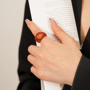 Détail d'une bague en résine ambre avec pétales séchés sur l'index et blazer noir