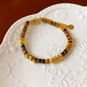 Macro shot of tiger eye stone bracelet with golden spacers on a vintage ceramic plate