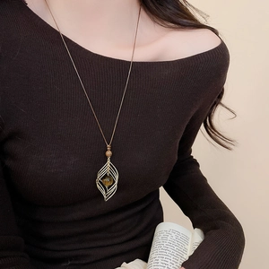 Detail of a vintage golden hollow leaf pendant with a brown tiger eye bead on a cord necklace