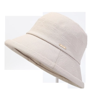 Détail d'un chapeau cloche beige avec texture plissée et plaque en métal doré