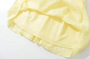 Dettaglio dell'orlo del vestito giallo chiaro con ricamo a giorno e fodera morbida