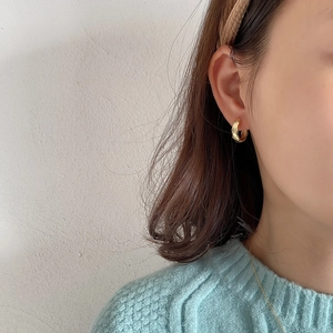 Close-up of golden geometric quilted pattern small hoop earrings worn on earlobe