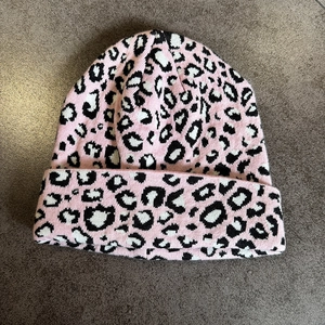 Flat lay detail of pink leopard jacquard knit beanie on textured background
