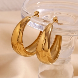 Detailed close-up of chunky gold-plated crescent hoop earrings on a crystal glass stand