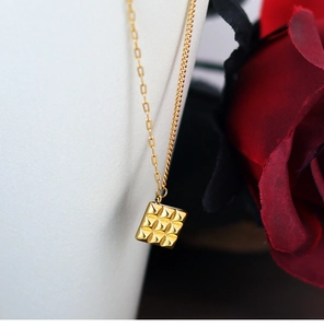 Detail of square gold-plated chocolate cube pendant with pyramid texture on a fine chain
