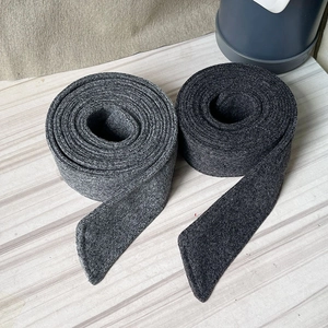 Detail view of thick grey felt tapes with reinforced stitched edges on wood surface