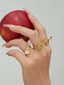 Detail von 18K vergoldeten Gitarrenringen an der Hand, die einen roten Apfel hält