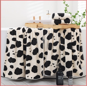 Detailed view of soft coral fleece towels with cow print pattern on a white bathtub
