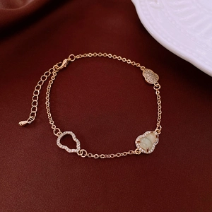 Macro detail of golden gourd bracelet with green gemstone and pavé stones on red velvet