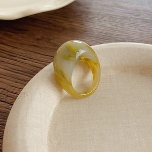 Détail d'une large bague en résine avec texture ambre marbrée sur un plateau beige