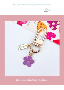 Close-up of golden metal keychain with purple flower charm and lobster clasp detail