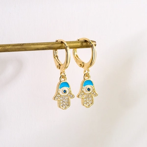 Gold Hamsa Hand earrings with blue enamel eye and zircon crystals on white background