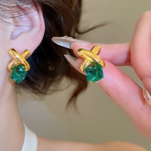 Detail of silver needle earrings with green crystal and gold crisscross metal base