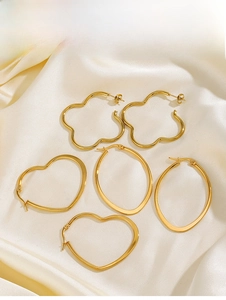 Macro detail of gold-plated hoop earrings in heart and flower shapes on silk background