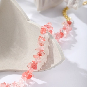 Macro shot of natural pink strawberry quartz beads and gold chain on a textured prop