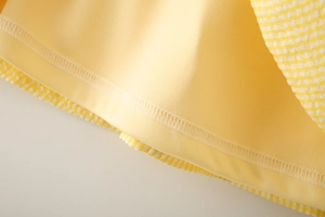 Macro shot of yellow gingham cotton dress showing high-quality stitching and seam detail