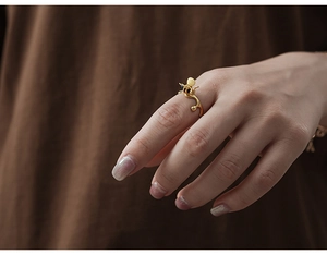 Detail of a gold bee-shaped ring with natural agate on a finger with a textured backdrop