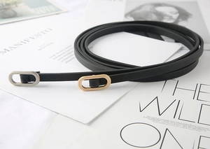 Detail of thin black belts with oval gold and silver buckles on fashion magazine background