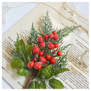 Detail shot of artificial red berry stem with frosted leaves on vintage paper backdrop