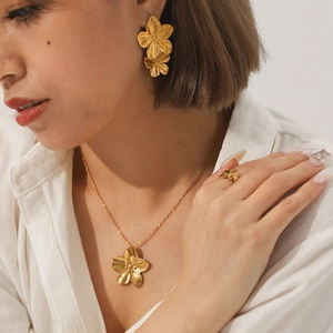 Golden flower jewelry set with necklace earrings and ring on model wearing white shirt