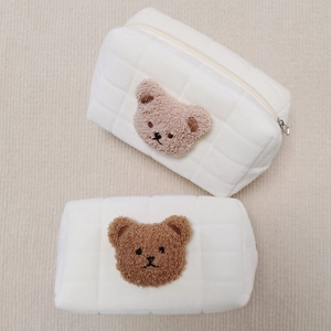 Close-up of quilted cream pencil cases with cute embroidered bear patches and zippers