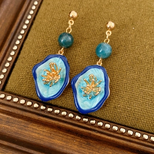 Close-up of vintage gold flower earrings with blue enamel and teal beads on dark fabric