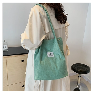 Detail view of a mint green corduroy tote bag worn over the shoulder in a cozy room