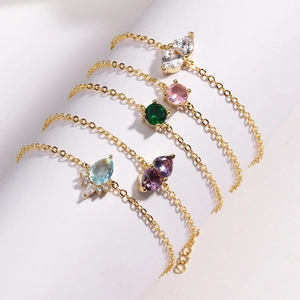 Detail of five gold chain bracelets with colorful gemstones wrapped on a white cylinder