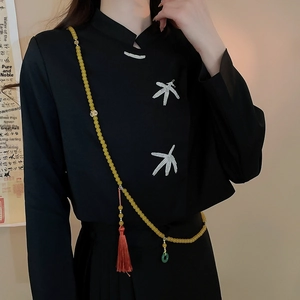 Détail d'un long collier de perles jaunes avec pompons en soie sur un haut cheongsam