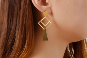 Close-up of a model wearing geometric gold earrings with square and triangle drops