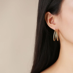 Macro shot of gold-plated triple layer twisted hoop earrings on model ear lobe