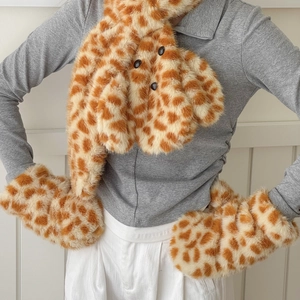 Detailed view of plush giraffe print winter scarf and matching mittens on a model