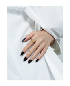 Detail of gold bow ring and cubic zirconia band set styled on hand with black nails