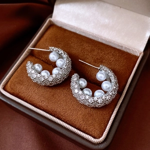 Close-up of silver C-shaped earrings with pearls and crystals in a velvet box
