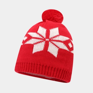 Detailed close-up of a red knitted beanie with white snowflake patterns and a pom-pom top