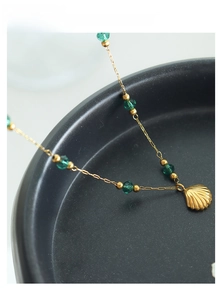 Close-up of gold shell pendant necklace with faceted green crystal beads on black tray