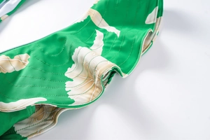 Detail of ruffled edges and green botanical print on a one-piece swimsuit fabric