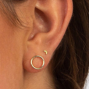 Close-up of minimalist gold crescent moon and tiny hoop stud earrings on ear