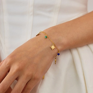 Detail of a gold stainless steel bracelet with a star pendant and colorful beads on a wrist