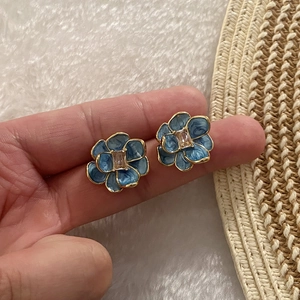 Elegant blue floral stud earrings with gold trim and crystal center held by hand