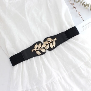 Detail of black elastic belt with golden leaf buckle on a white dress for women