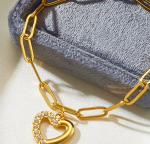 Macro shot of gold paperclip chain bracelet with a heart pendant featuring pavé zircon
